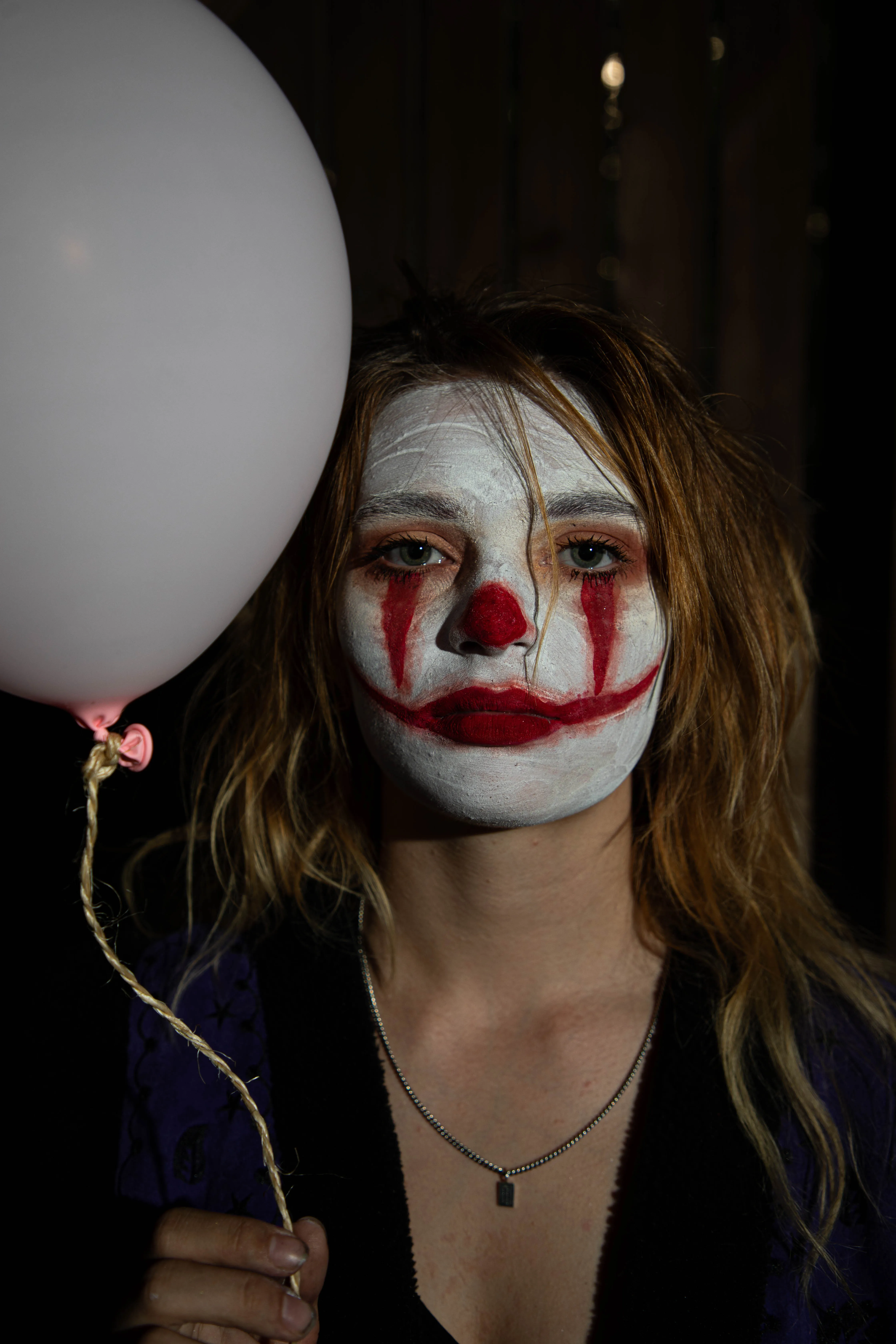 Een jonge vrouw met een clownsgezichtsmakeup en een roze ballon kijkt recht in de camera.