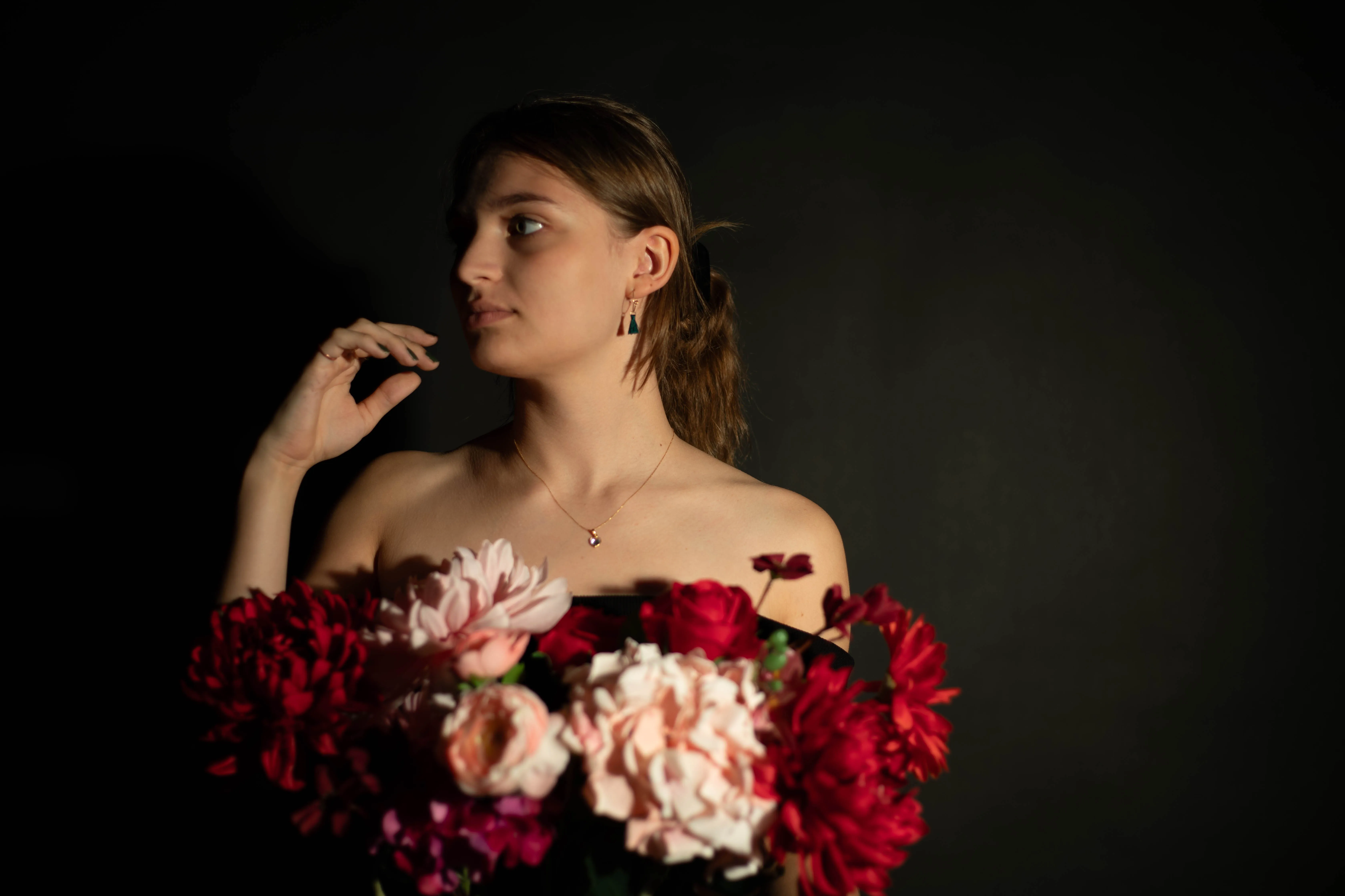 Een jonge vrouw in een zwarte achtergrond poseert met een boeket kleurrijke bloemen.