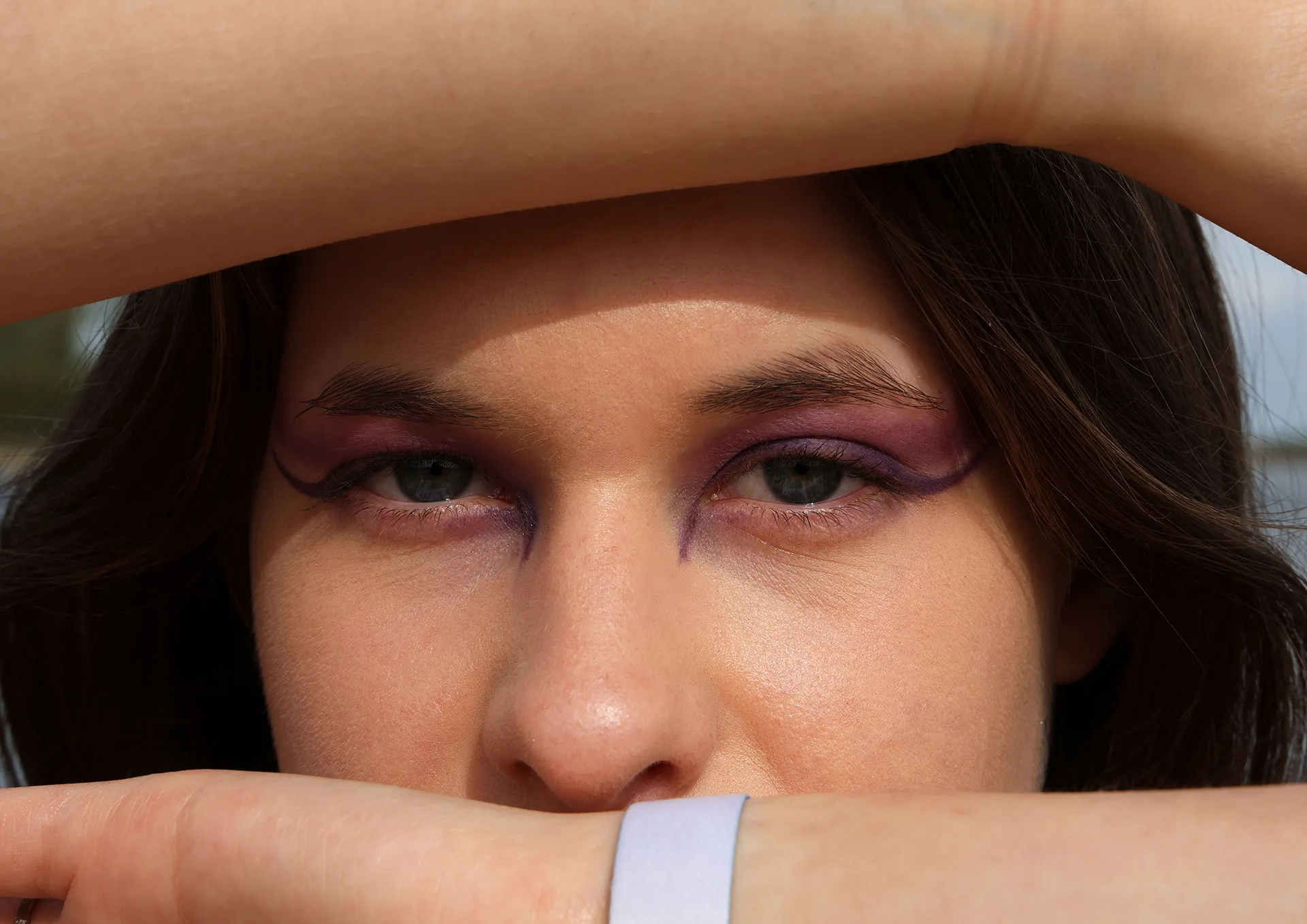 Close-up van een vrouw met opvallende paarse oogmake-up die haar arm voor haar gezicht houdt.