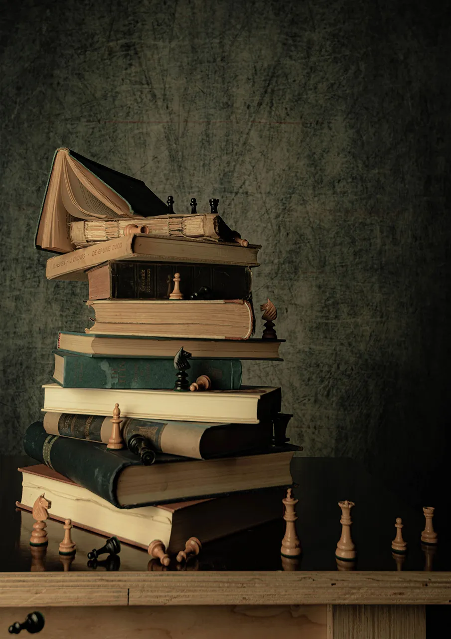 Een stapel oude boeken met daarop een schaakspel en enkele schaakstukken eromheen.